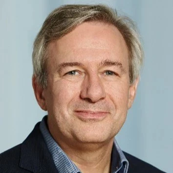 CLose up of Frank Schimmelfennig, wearing a dark suit jacket and a blue shirt, smiling at the camera